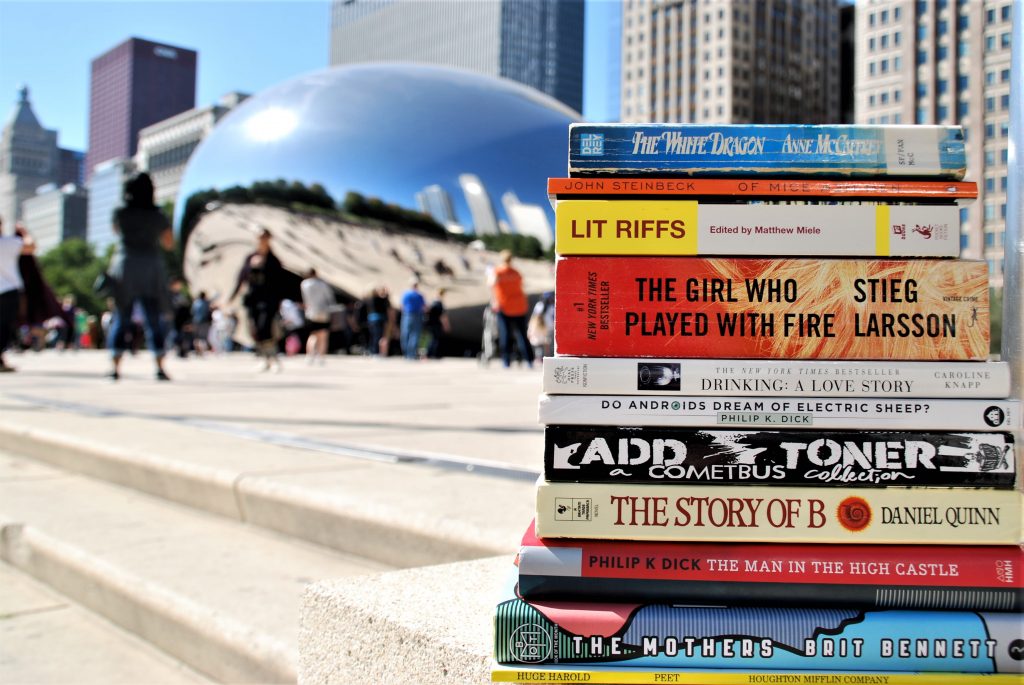 Stack of books in focus in the foreground, with Chicago's Cloud Gate in the background