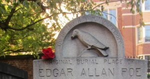 Edgar Allan Poe's grave stone, which features a carved raven, with a red rose on top of it.