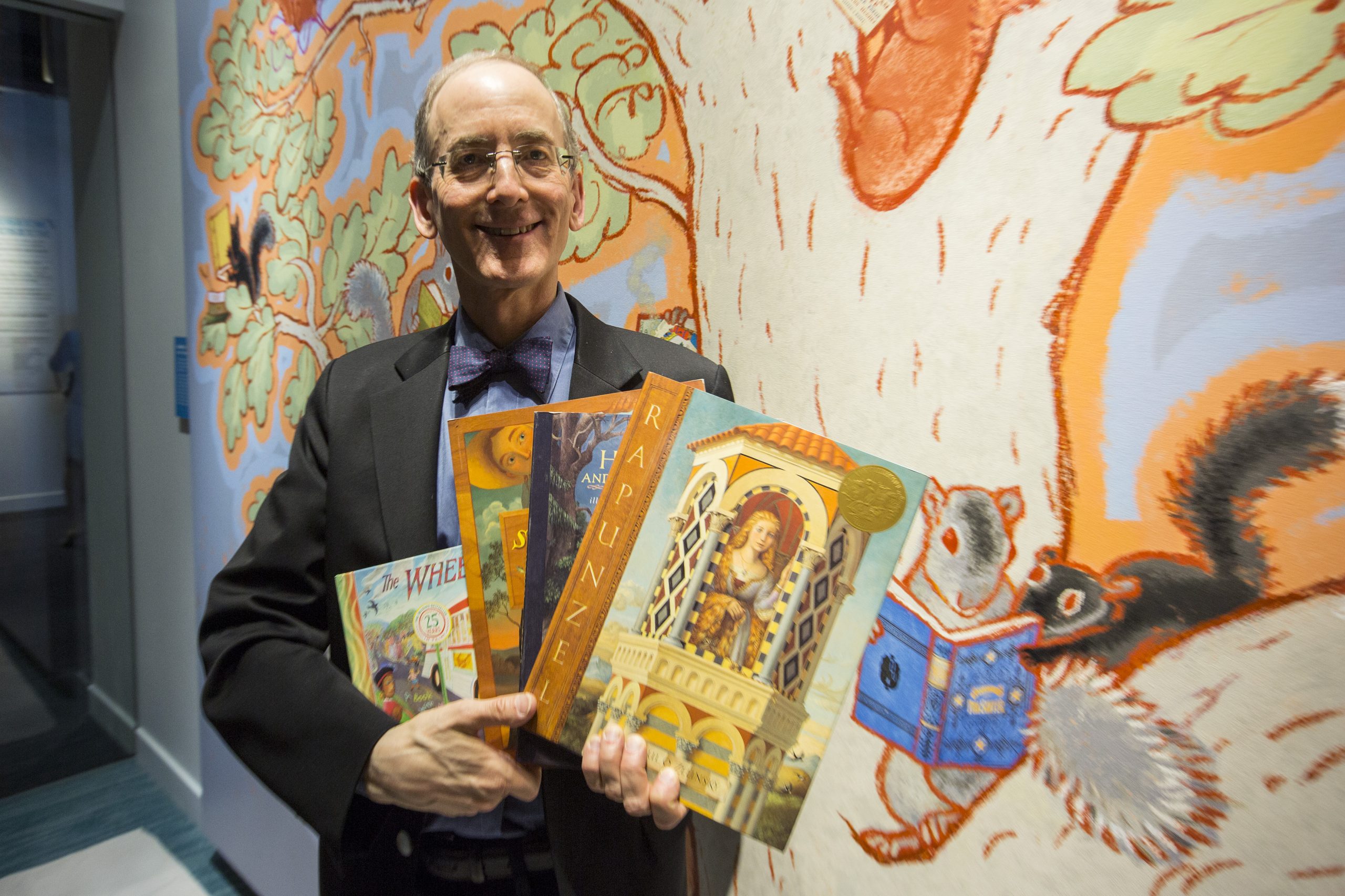 Paul O. Zelinsky standing in front a mural of a tree in the American Writers Museum