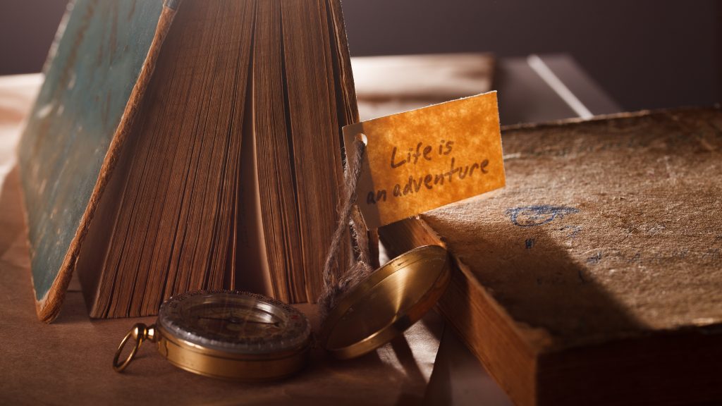 An old book and open compass with the label "life is an adventure"