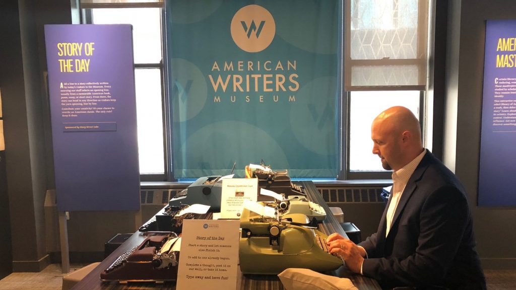 A man in a blazer uses typewriters at the American Writers Museum