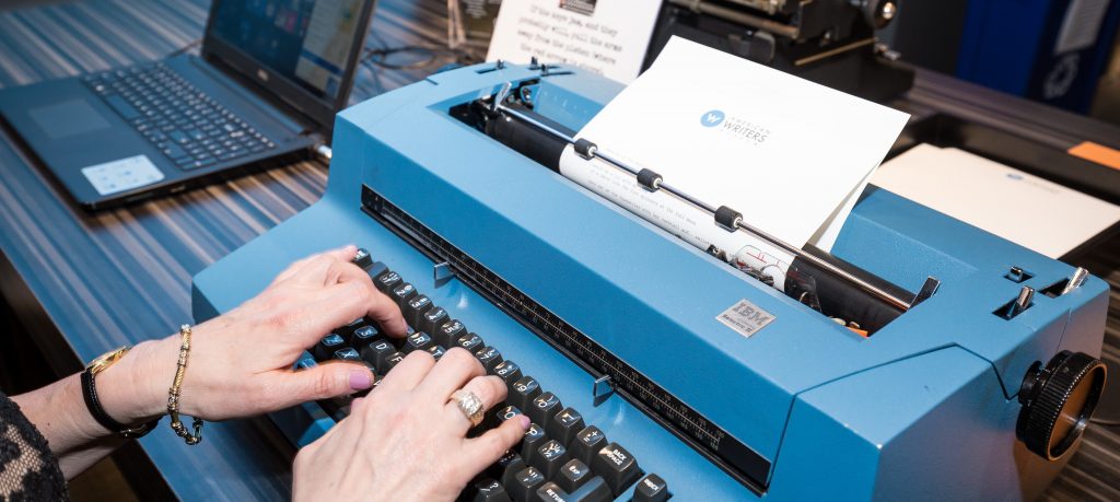 A visitor's hands typing on a large blue IBM typewriter at the American Writers Museum