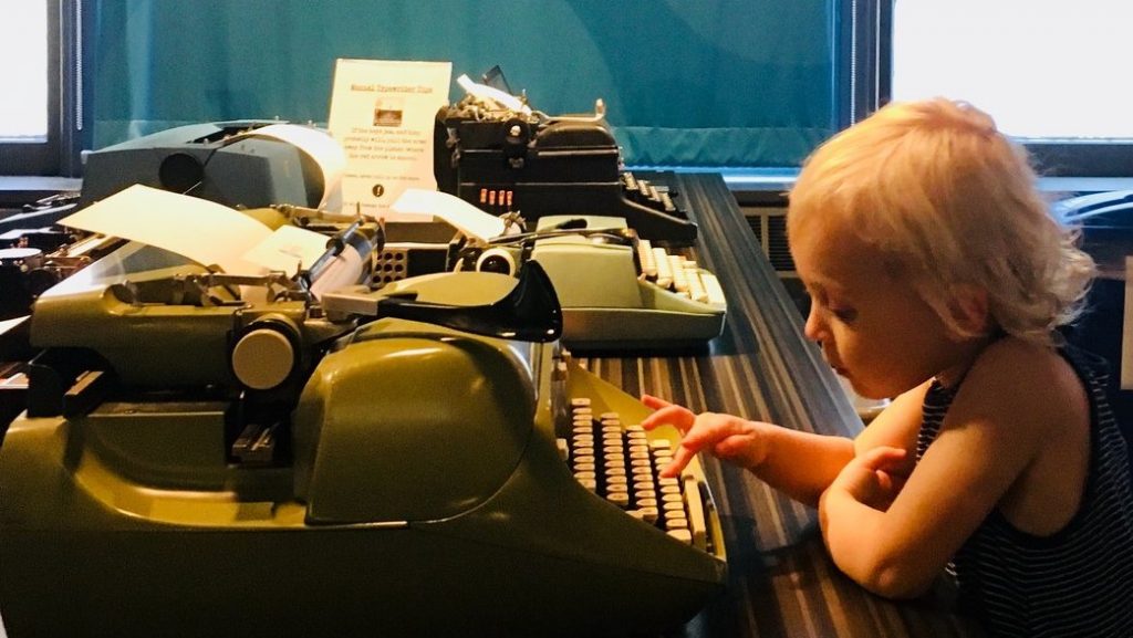 small child typing on a green typewriter at the Story of the Day exhibit