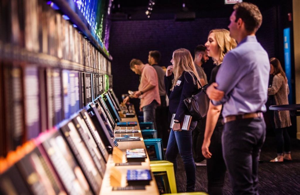 A group of visitors interact with the American Voice timeline in the Nation of Writers Gallery at the American Writers Museum in Chicago, IL. A blonde woman in a black sweater in the middle ground is the focus of the photo.