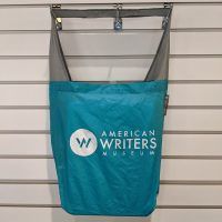 A teal tote bag with the American Writers Museum logo in white on the front.