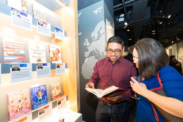 2 people read a book together in the My America: Immigrant and Refugee Writers Today exhibit at the American Writers Museum in Chicago, IL