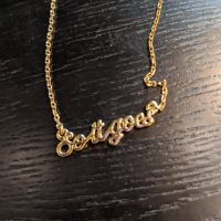 A gold necklace with pendant words reading "So it goes"