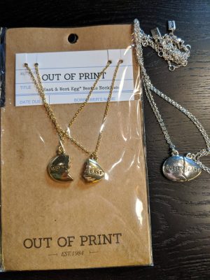 A pair of necklaces with pendants in the shape of a broken egg that fit together. One pendant says "West" and the other says "East." Shown in both silver and gold.