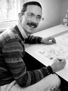Photo of Bill Watterson drawing at desk and smiling