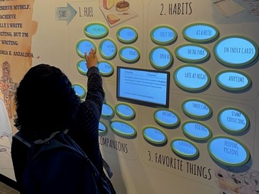 A student on a field trip at the American Writers Museum selects an option on a touch-wall that shows famous writers' habits.