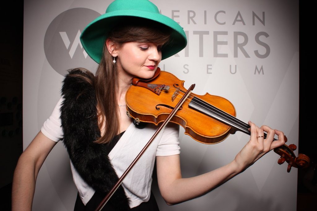 A woman wearing a teal hat playing the violin at the American Writers Museum