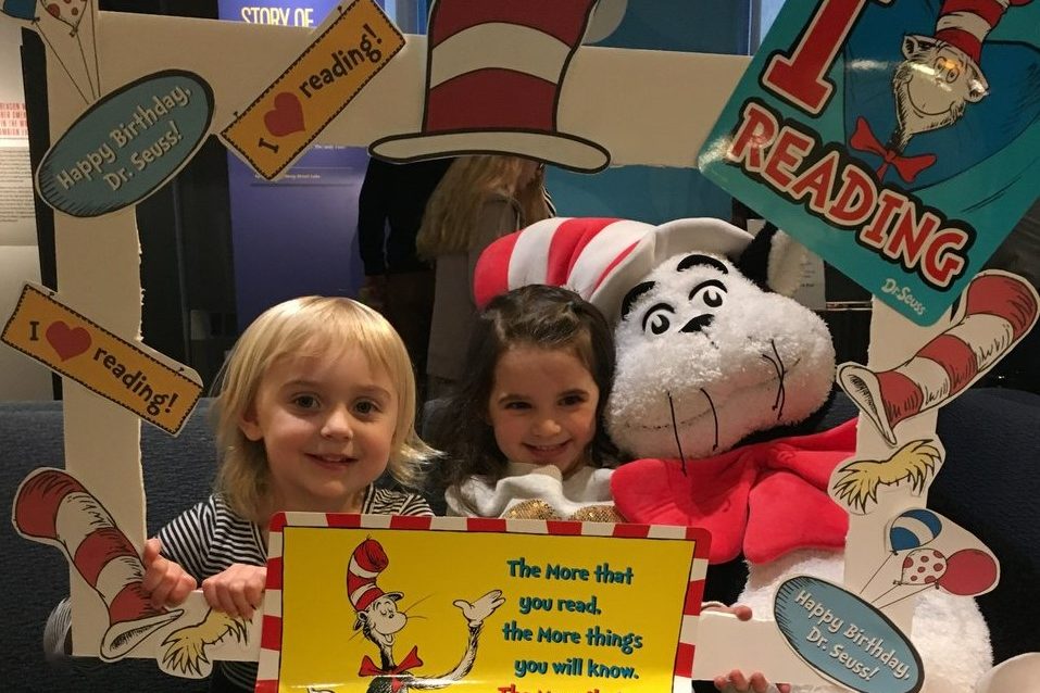 Two children pose on a couch at the American Writers Museum holding a frame that has The Cat in the Hat and "I love reading" written on it.