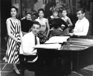 Carol Lawrence, Stephen Sondheim, Leonard Bernstein, and cast members around the piano rehearsing for West Side Story, 1957. (Photo by Friedman-Abeles)