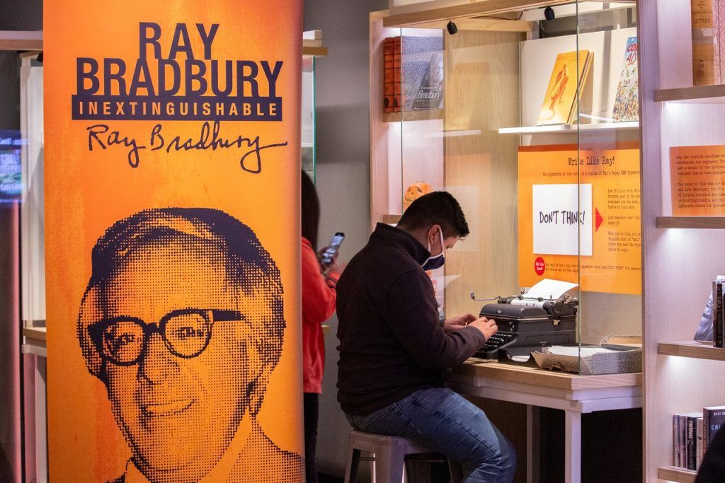 A student on a field trip at the American Writers Museum typing on a typewriter with a sign in the foreground that reads "Ray Bradbury: Inentinguishable"
