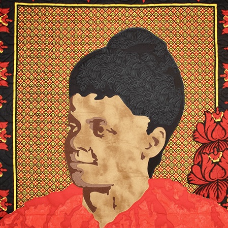 A quilt depicting Ida B. Wells in a red dress on a red, yellow, and brown background.