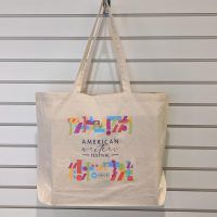 An off-white canvas tote bag with a rainbow colored punctuation design surrounding the words 